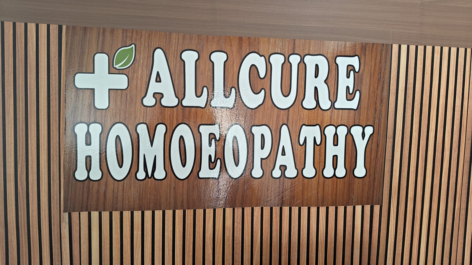 Allcure Homoeopathy clinic signboard with the brand name on a wooden panelled wall